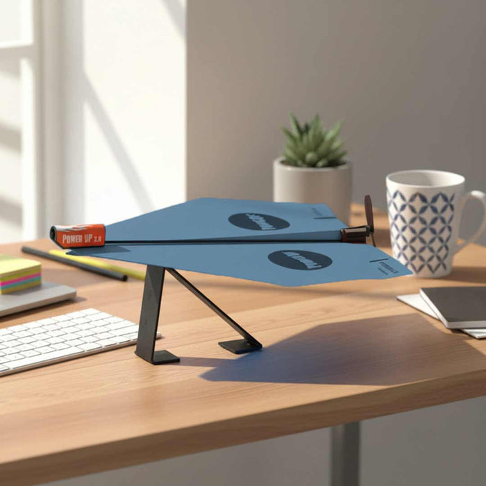 Power Up plane Blue on an adjustable desk stand on a wooden desk with a mug and plant in the background