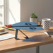 Power Up plane Blue on an adjustable desk stand on a wooden desk with a mug and plant in the background