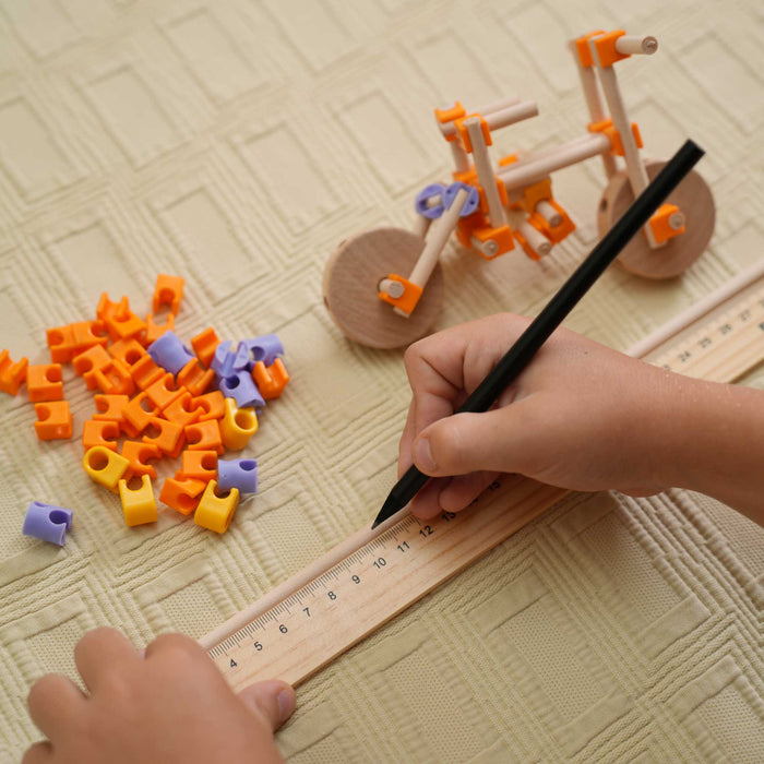 Beaver Construction Kit 100pc Child's hand using a ruler and pencil with building blocks on a textured surface