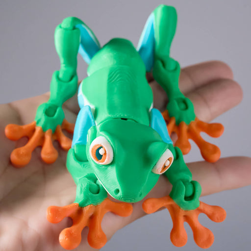 3D hebee jeebies Toy frog with green body, orange legs, and blue accents on a wooden surface