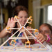 Two children playing with a Beaver wooden tower made of sticks and connectors.