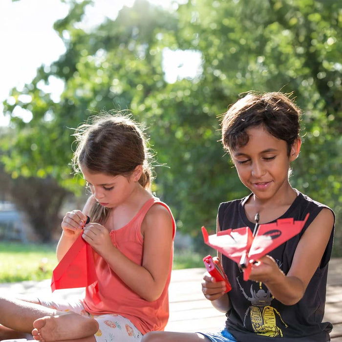 Two children playing with power up toy airplanes outdoors on a sunny day.