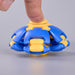 A close-up of a blue and yellow plastic toy being pressed down by a human finger, set against a plain light gray background. Fidgit Sphere Spinner