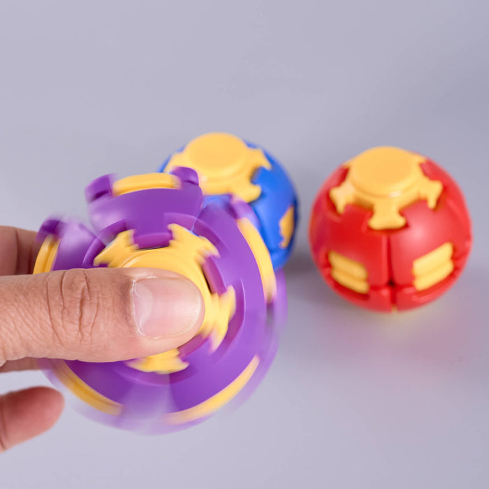 A hand is holding a purple and yellow spinning ball toy, with two more ball toys in blue and red resting on a light gray background. Fidgit Sphere Spinner