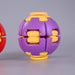 A purple and yellow plastic ball-shaped puzzle toy shown on a light gray studio background, with part of a red version visible at the left edge. Fidgit Sphere Spinner