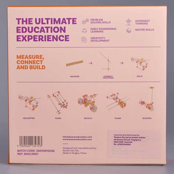 The back of a product box for an educational toy set, featuring a pale pink background with purple and orange text, diagrams, and photos of small metal construction toys including a helicopter, kraxak, bicycle, plane, and scooter.