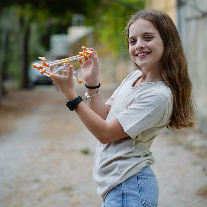 Young girl holding a Beaver wooden toy gun outdoors with a blurred background