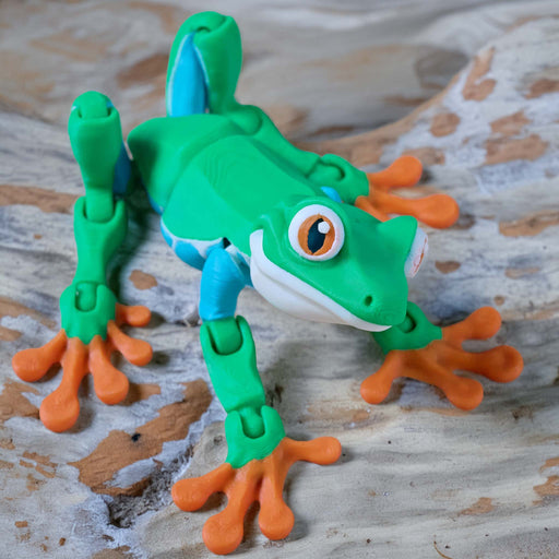 3D hebee jeebies Toy frog with green body, orange legs, and blue accents on a wooden surface