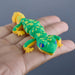 Green and yellow toy Gecko held in a hand against a gray background