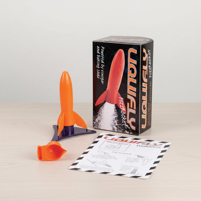 A heebie jeebies toy rocket set on a light wood tabletop against a white wall, including an orange and purple rocket, its retail box, and an instruction sheet.